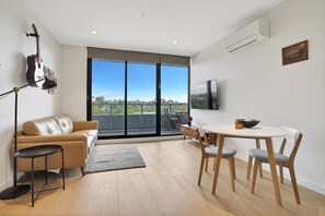 Een moderne woonkamer met een bank, een eettafel met stoelen, een gitaar en een groot raam met uitzicht op de stad.