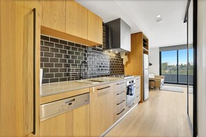 Een moderne keuken met houten kastjes, een zwart betegelde spatwand en uitzicht op de omgeving door grote ramen.