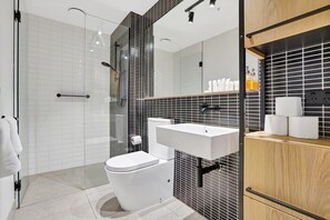Een moderne badkamer met een glazen douchecabine, een wit toilet en een wastafel met een zwarte spatwand.