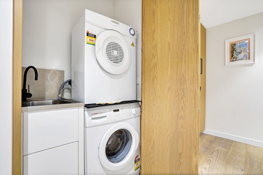 A compact laundry area with a Bosch washing machine and dryer, a sink, and a wooden door.