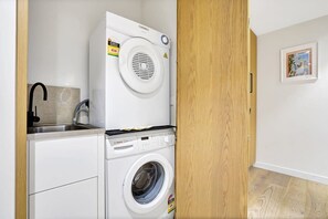 Een kleine wasruimte met een Bosch wasmachine en droger, een spoelbak en een houten deur.