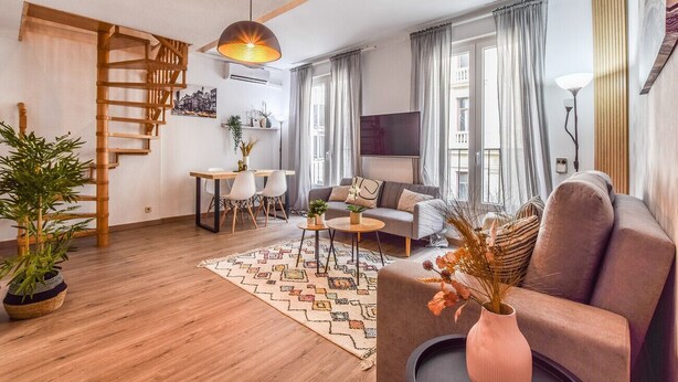 A modern living room with a wooden staircase, a sofa, a coffee table, and a dining area. - Collection Plaza España (Madrid)