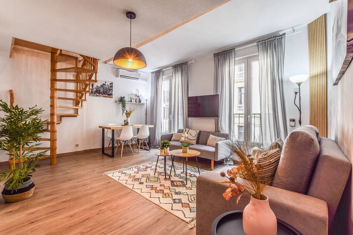 Una sala de estar moderna con una escalera de madera, un sofá, una mesa de centro y un comedor.
