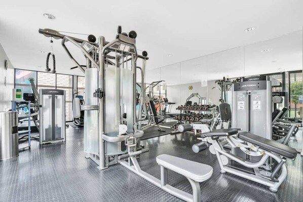 A modern gym with various exercise equipment, including a bench press, dumbbells, and weight machines. - Spacious&Cozy 2 bedroom City Point Melbourne Apt (Melbourne)
