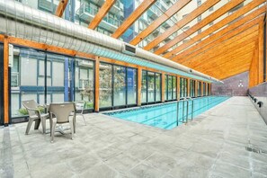 Una piscina interior con cerramiento de vidrio, vigas de madera y suelo de baldosas.