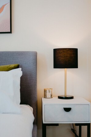 A neatly made bed with white linens and a green pillow, a bedside table with a lamp, and a small decorative item on the table. - Spacious&Cozy 2 bedroom City Point Melbourne Apt (Melbourne)