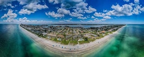 An aerial view of a coastal town with a beach, houses, and a clear sky.