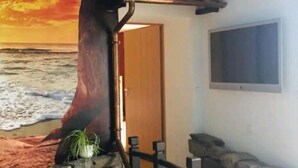 Una habitación con un mural de playa, una puerta de madera, un muro de piedra y una pequeña zona ajardinada con una planta y un florero.