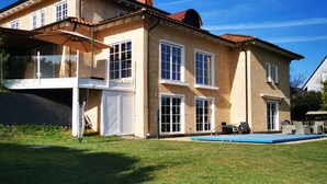 Una casa de dos pisos con un jardín delantero amplio, piscina y un patio cubierto.
