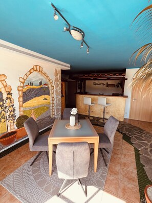 Un comedor con mesa y sillas, una cocina al fondo y un mural en la pared.