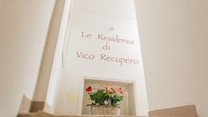 A white wall with the text "Le Residenze di Vico Recupero" and a small wicker basket with red flowers. - Residenza Vico Recupero by Wonderful Italy (Polignano a Mare)