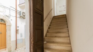 A narrow staircase with a wooden door at the bottom, a white wall with a sign, and a stone-paved ground. - Residenza Vico Recupero by Wonderful Italy (Polignano a Mare)