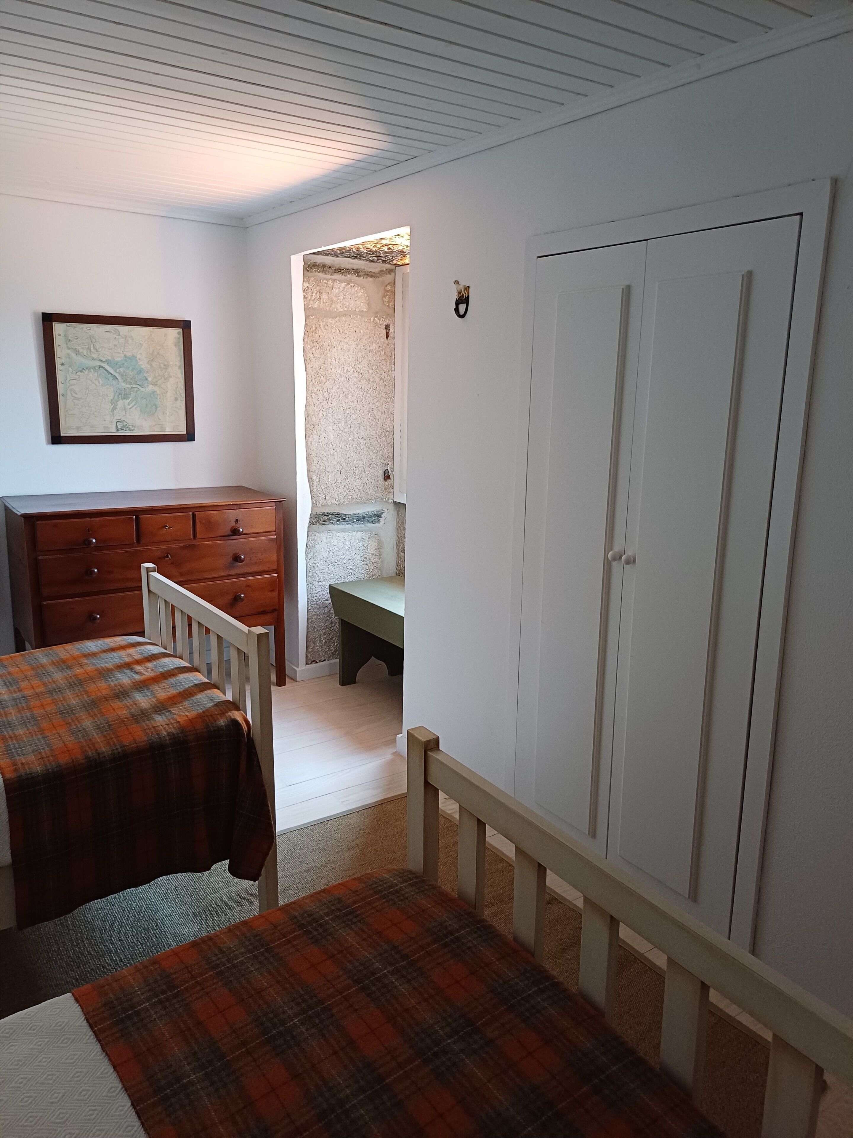 A bedroom with a wooden dresser, a bed with a plaid blanket, a white wardrobe, and a map on the wall.