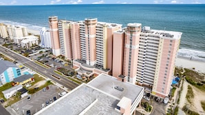 Un hotel moderno de gran altura con varios pisos, estacionamiento y vistas a la playa y al océano.