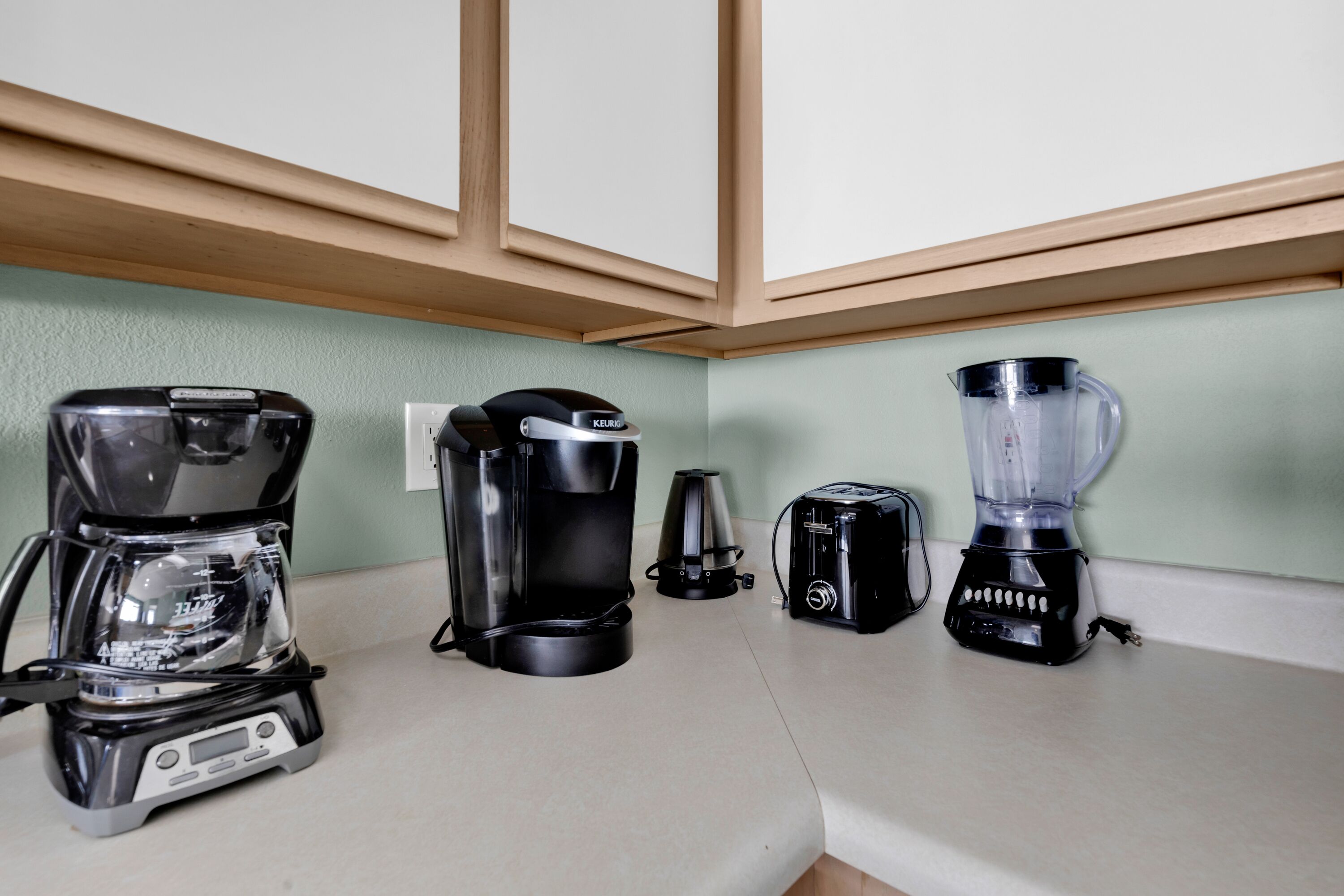 Een aanrecht met een koffiezetapparaat, een Keurig, een broodrooster en een blender.