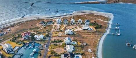 An aerial view of a coastal residential area with multiple houses, a marina, and a beach.