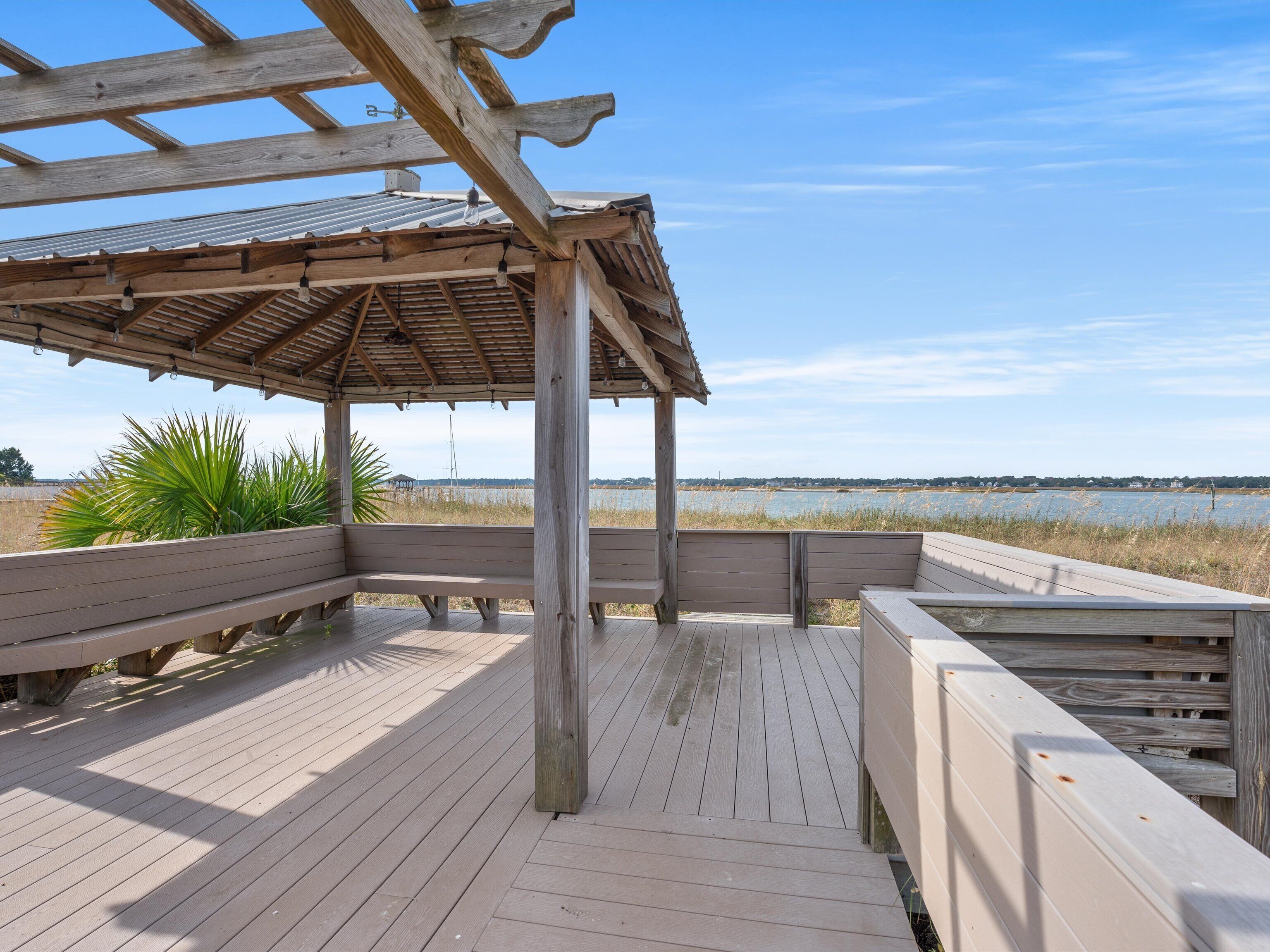 A wooden deck with benches and a pergola, overlooking a body of water.