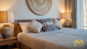 A neatly made bed with a patterned pillow, two bedside lamps, and a large woven wall hanging. - NHOA 112A Lux 2BR Condo Plunge Pool in Aldea Zama (Tulum)