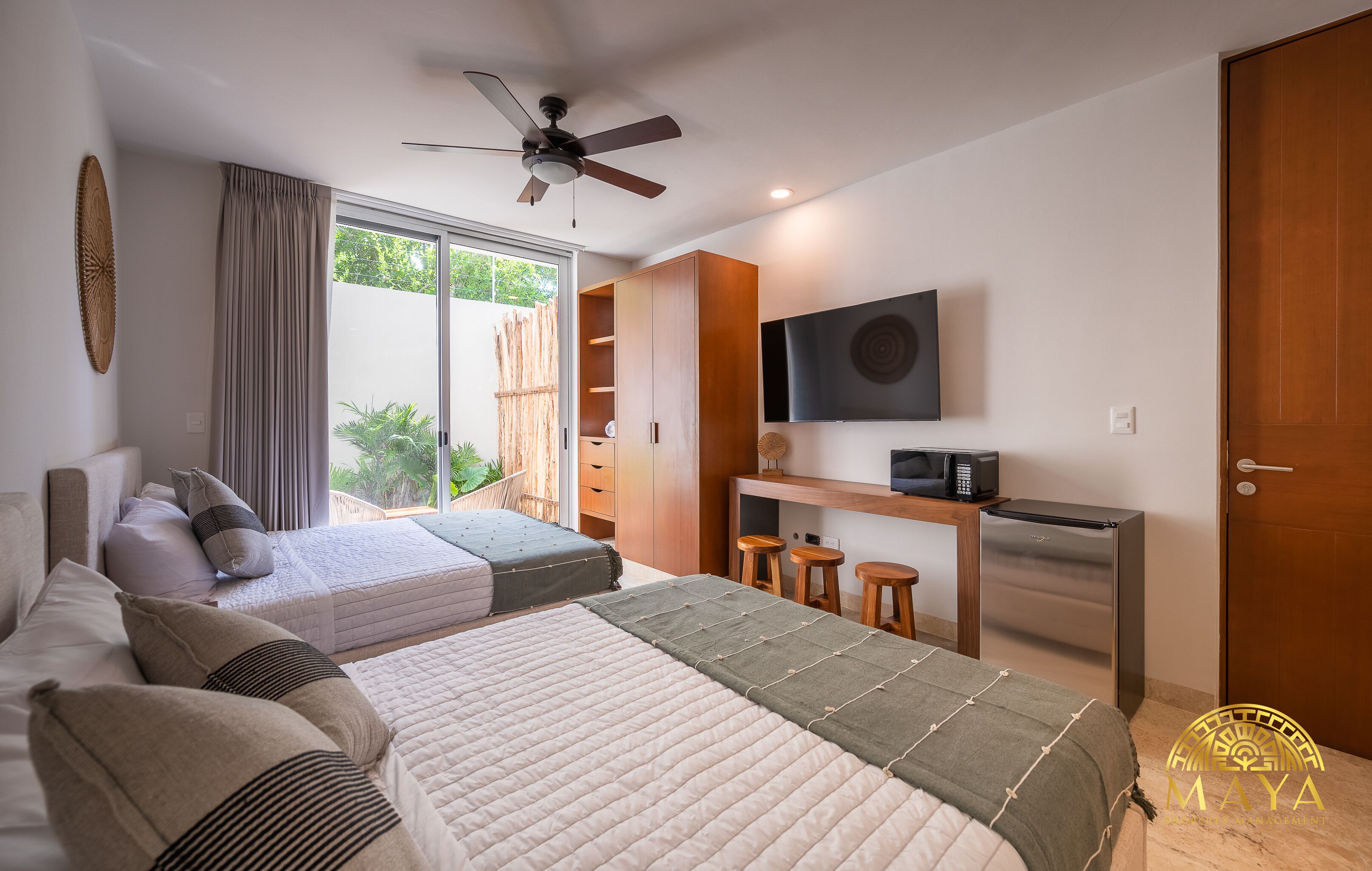 A modern bedroom with two beds, a desk, a TV, and a refrigerator.