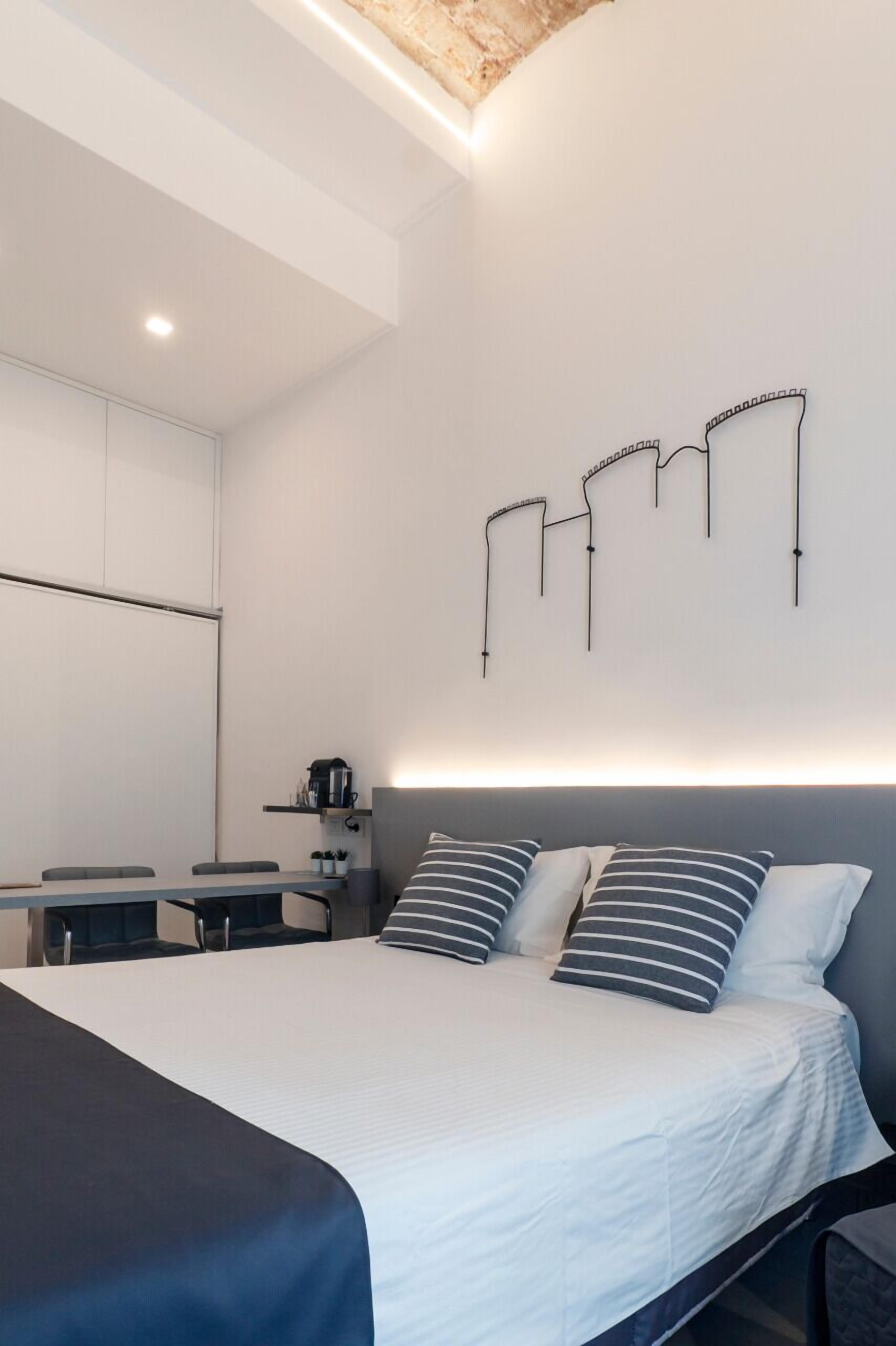 Un dormitorio moderno con cama, mesitas de noche, escritorio y una lámpara fijada en la pared.