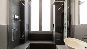 A modern bathroom with a glass shower enclosure, a large bathtub, and a vanity with a sink. - VESUCHARME Suite Luxury Room (Naples)
