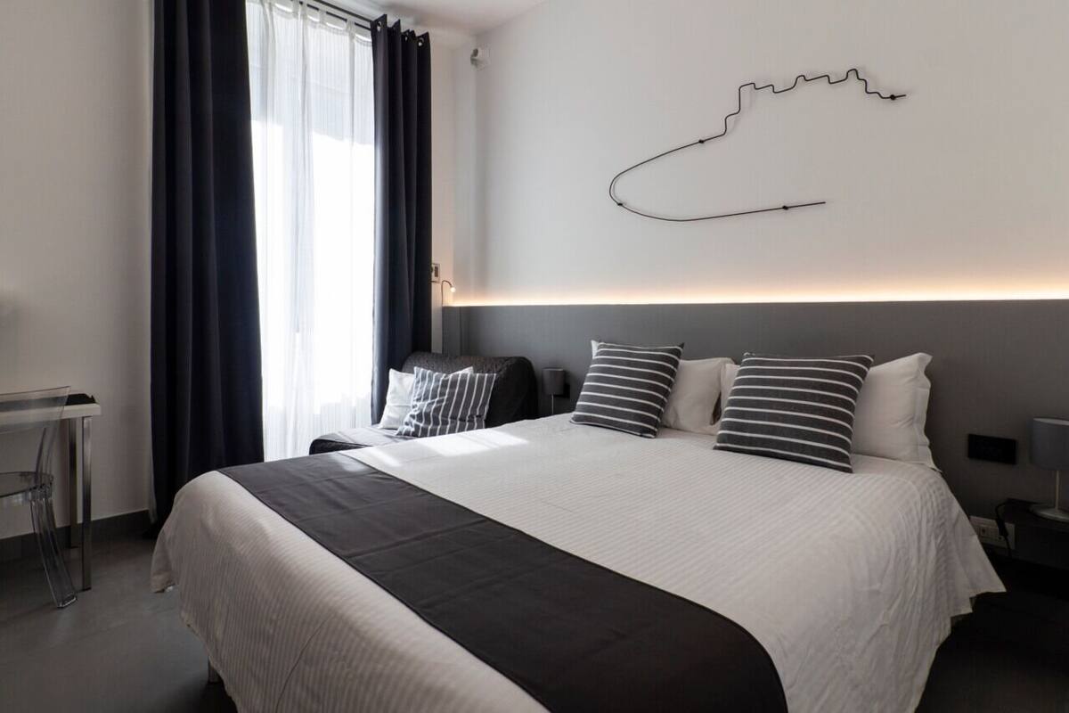 A modern hotel room with a large bed, a desk, and a wall-mounted artwork.