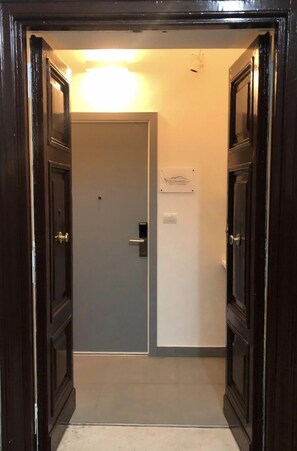 A hallway with a door leading to a room, a sign on the wall, and a light fixture above the door. - VESUCHARME Suite Luxury Room (Naples)