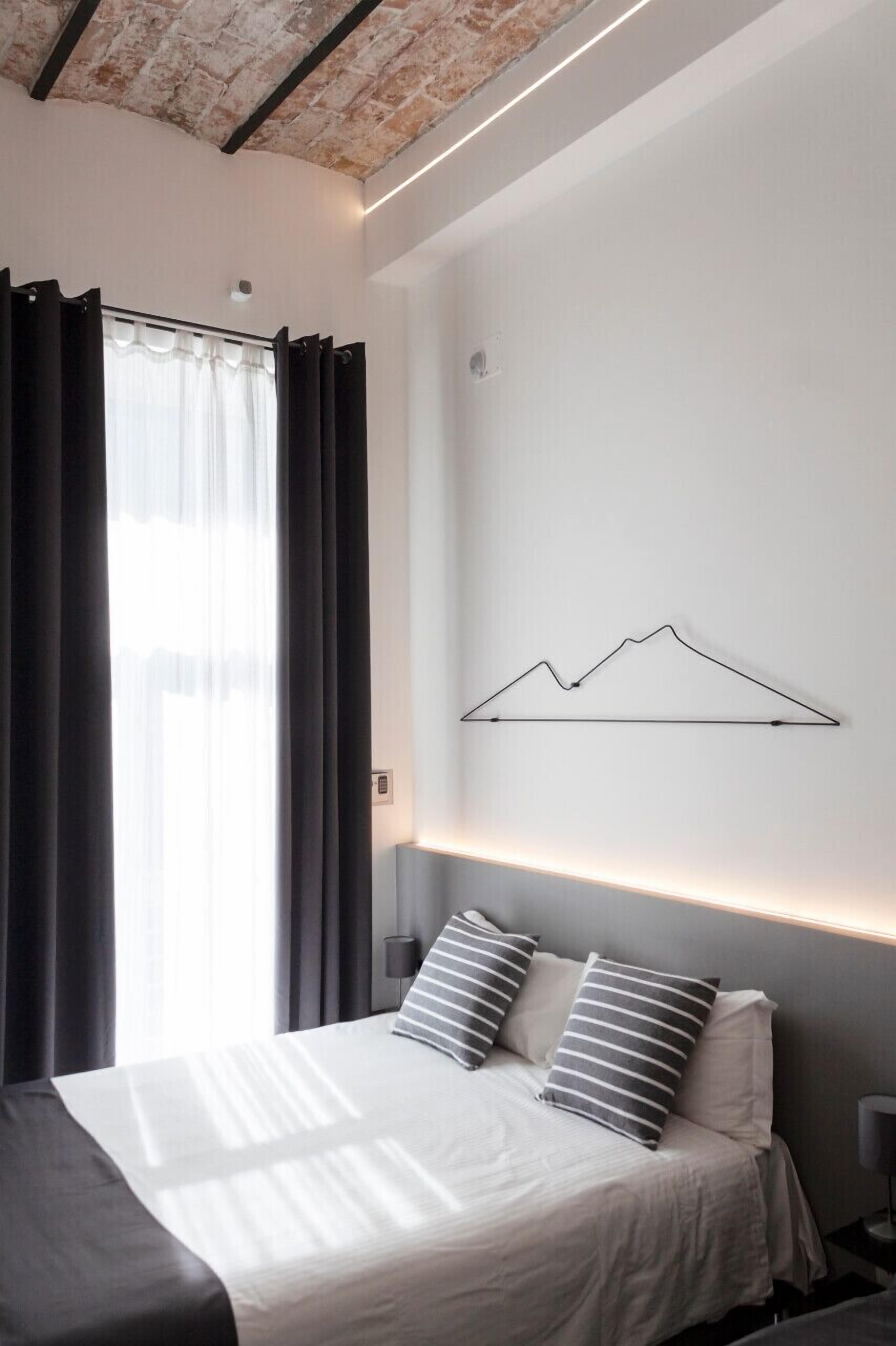 Ein modernes Schlafzimmer mit Bett, Vorhängen und einer wandmontierten Lampe.