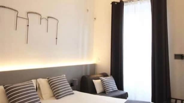 A hotel room with a large bed, a bedside table, a lamp, and a window with curtains. - VESUCHARME Suite Luxury Room (Naples)