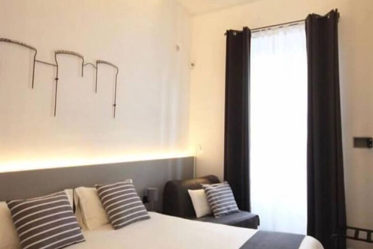 A hotel room with a large bed, a bedside table, a lamp, and a window with curtains.
