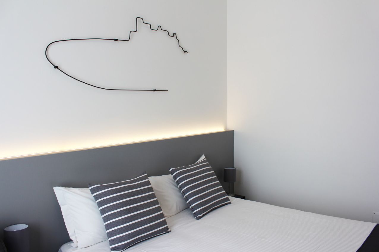 Een moderne slaapkamer met een bed, twee gestreepte kussens, een wandlamp en een eenvoudige tekening.