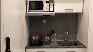 A compact kitchenette with a microwave, a sink, and cabinets. - VESUCHARME Suite Luxury Room (Naples)