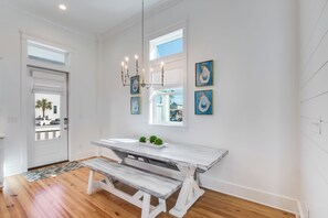 A dining area with a white table and bench, a chandelier, and framed artwork on the wall.
