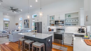 Une cuisine moderne avec des meubles blancs, des appareils en acier inoxydable et un îlot central doté de tabourets.