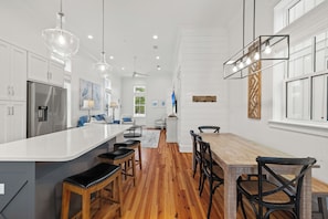 A modern kitchen with a central island, wooden flooring, and pendant lighting.