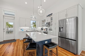 A modern kitchen with white cabinetry, a stainless steel refrigerator, and a central island with bar stools.