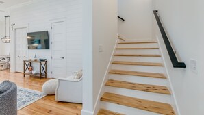 A modern interior with a staircase, a flat-screen TV mounted on a white door, and a dining area with wooden flooring and a patterned rug. - BVR 40 - Isle Be Back by Liquid Life (Orange Beach)