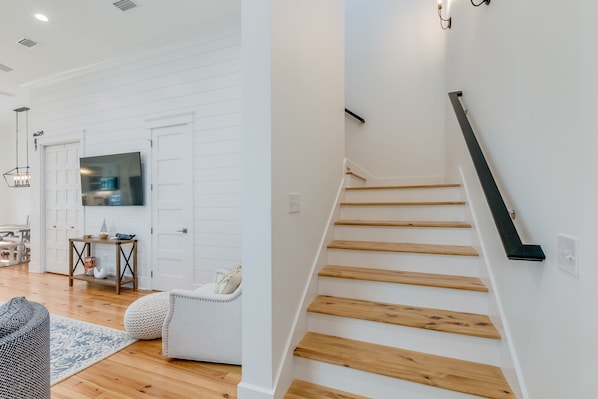 A modern interior with a staircase, a flat-screen TV mounted on a white door, and a dining area with wooden flooring and a patterned rug.