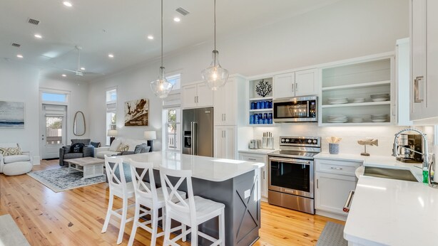 A modern kitchen with white cabinetry, stainless steel appliances, and a central island with bar stools. - BVR 40 - Isle Be Back by Liquid Life (Orange Beach)