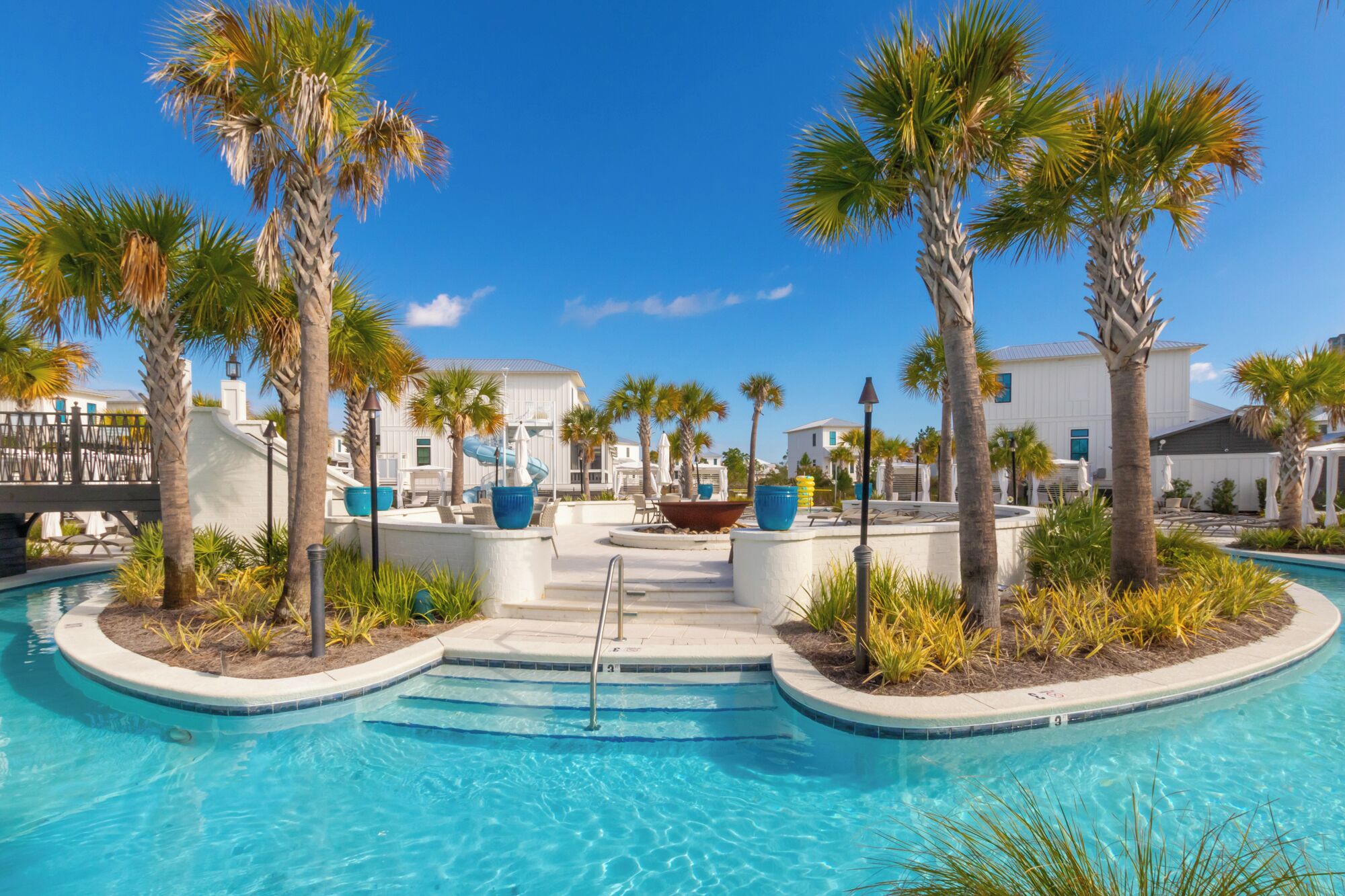 A pool area with palm trees, a water slide, and a building with a white facade.