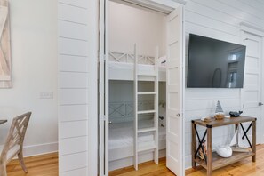 A room with a bunk bed, a wooden chair, a small table with a decorative item, and a television on the wall.