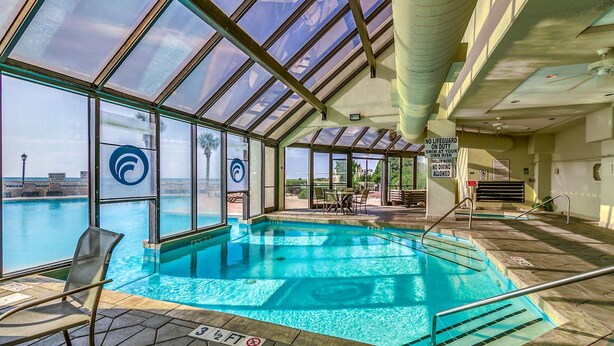 An indoor swimming pool with clear glass walls, a view of the city, and a no lifeguard sign. - Ocean Creek Kk-14 2 Bedroom Condo by RedAwning (Myrtle Beach)