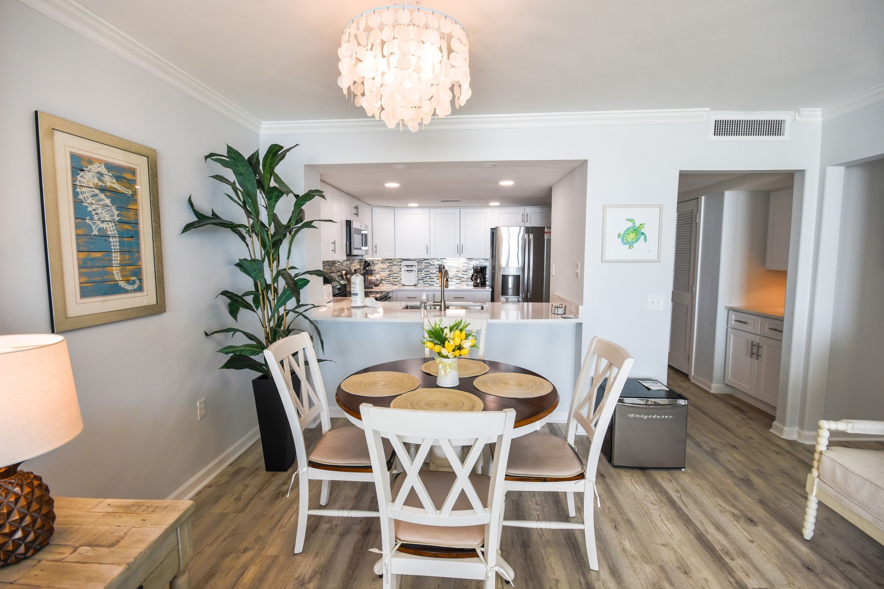 A dining area with a round table, white chairs, a chandelier, and a potted plant.