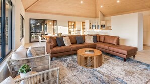 A modern living room with a large sectional sofa, wicker chairs, a coffee table, and a large window providing a view of the outside.