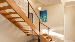A wooden staircase with a glass railing, a painting on the wall, and a light fixture.