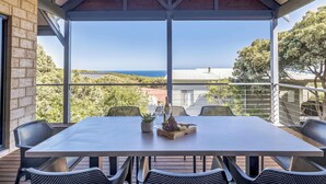 A covered outdoor dining area with a table set for two, featuring a bottle of wine and a fruit platter.