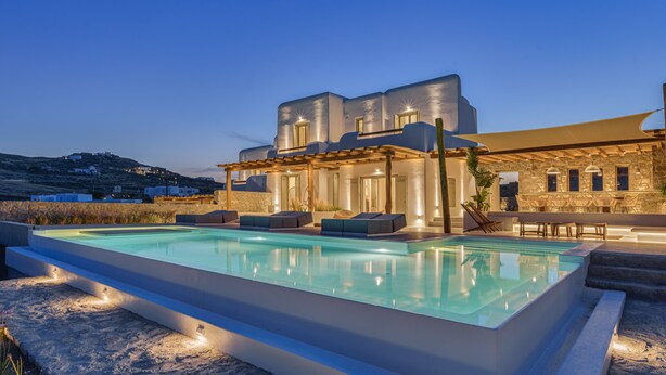 Ein moderner Poolbereich mit rechteckigem Pool, Sitzgelegenheiten im Freien und einem dahinterliegenden Steinhaus.