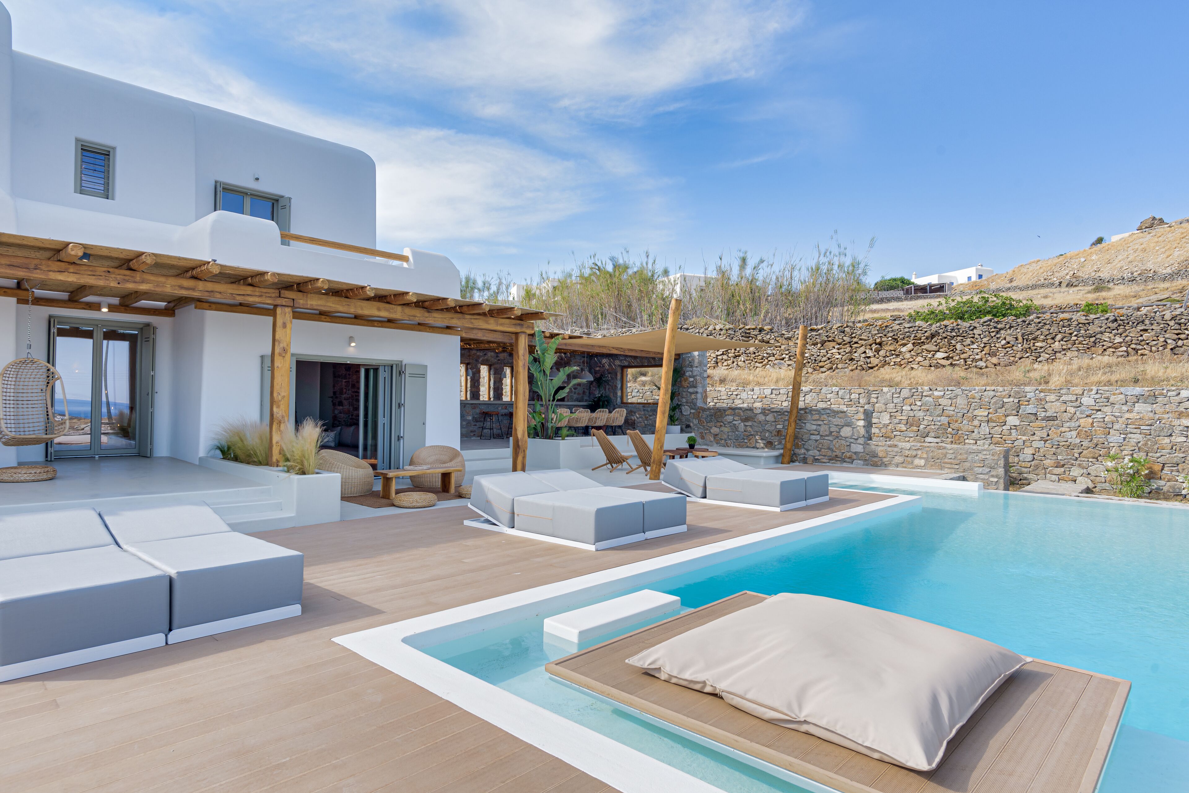 A modern outdoor pool area with white lounge seating and a stone wall backdrop.