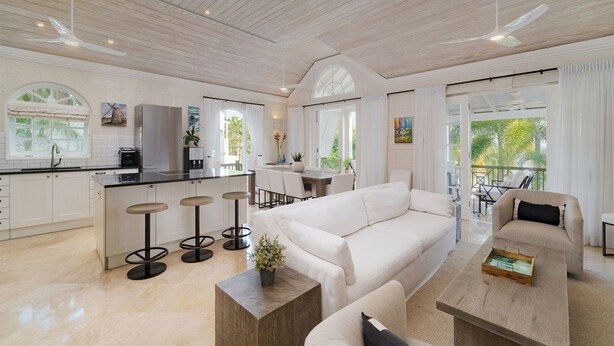 A spacious living area with a white sofa, a coffee table, and a kitchen area with a bar stool.