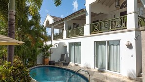 A two-story building with a swimming pool, outdoor seating, and a balcony with a green railing.
